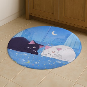 Può includere: Tappetino da bagno ovale blu con due gatti dei cartoni animati. Uno è nero, l'altro bianco. Entrambi dormono su uno sfondo blu con una luna crescente e stelle. Il tappetino è posizionato su un pavimento piastrellato.