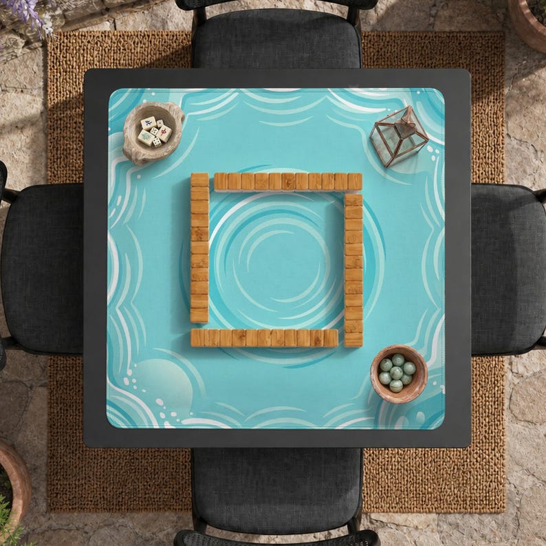 May include: Overhead view of a square Mahjong table set for play. The table has a light blue surface with a water wave design. Wooden tiles form a square in the center. Small bowls and a glass terrarium are on the table.