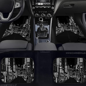 May include: Black and white car floor mats featuring a nighttime cityscape design. The mats depict a road leading through a city with illuminated signs and buildings. The mats are shown inside a car.