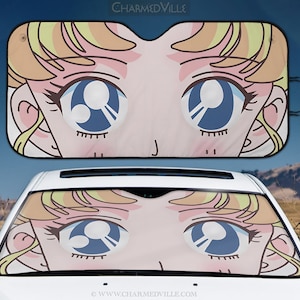 May include: A pink and yellow car sunshade featuring a cartoon anime character with large blue eyes. The character's hair is blonde and styled in a ponytail. The sunshade is designed to block sunlight from entering the car.