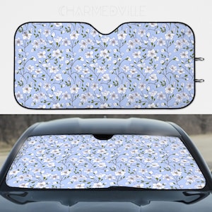 May include: A blue car sunshade with a white floral pattern. The sunshade has a black border and two black hooks on the top corners.