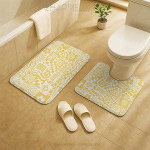 Könnte beinhalten: Ein Badezimmer-Set mit einer rechteckigen Badematte und einer U-förmigen Toilettenmatte, beide mit einem gelb-weißen Blumen- und geometrischen Muster. Zwei Paar cremefarbene Hausschuhe liegen auf dem Boden. Eine weiße Toilette und eine kleine Topfpflanze sind ebenfalls zu sehen.