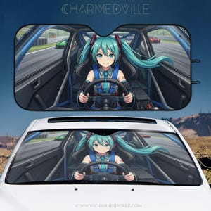 May include: Car sunshade featuring a cartoon anime character with long turquoise hair, wearing a racing suit, and driving a race car. The sunshade has a black interior design and the text "CHARMEDVILLE" at the top.