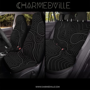 Peut inclure: Housses de si&egrave;ge de voiture noires avec un motif de carte topographique blanc. L'image montre les housses install&eacute;es dans une voiture, avec les si&egrave;ges avant et arri&egrave;re visibles. La marque "CHARMEDVILLE" est en haut.