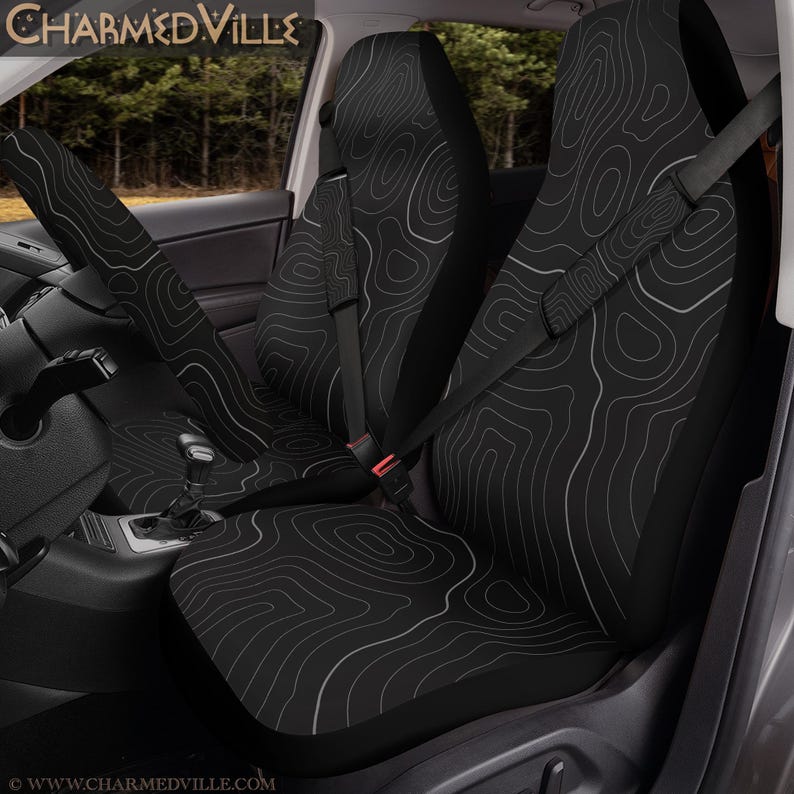 Peut inclure: Housses de si&egrave;ge de voiture noires avec un motif de carte topographique blanc. Les housses sont install&eacute;es dans un v&eacute;hicule, avec l'appui-t&ecirc;te et le dossier. La ceinture de s&eacute;curit&eacute; est visible. Le texte "CHARMEDVILLE" est en haut de l'image.