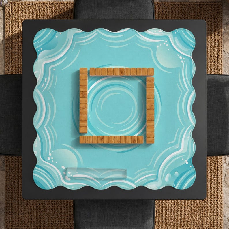 May include: A square, black coffee table with a light blue, wavy-edged surface. The surface features a water-like design with a wooden square in the center. The table is surrounded by gray cushions and a woven rug.