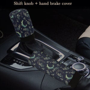 May include: Black and green car gear shift knob and handbrake cover with a moon and leaf pattern.