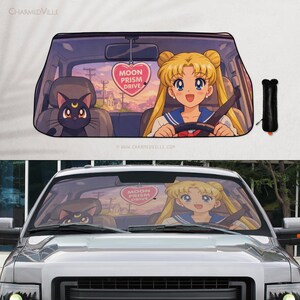 Op de afbeelding: Auto zonnescherm met een anime-stijl illustratie van een blond meisje dat een auto bestuurt, vergezeld van een zwarte kat. Een roze hartvormig ornament leest "Moon Prism Drive".