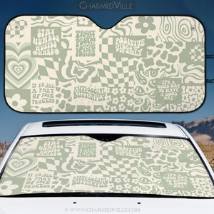 May include: A green and white car sunshade with a patchwork design featuring various patterns and text, including "Stay Humble Hustle Hard", "Treat People With Kindness", "Positive Vibes Only", "It is all a part of the process", "Anti-social Butterfly", and "It's a good day to have a good day".