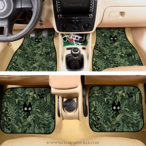 May include: A set of two black car floor mats with a green leafy pattern and black cats peeking out from the leaves. The mats are designed to fit the front seats of a car.