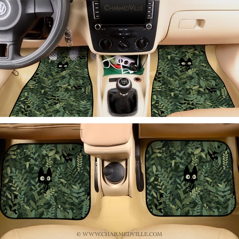 May include: A set of two black car floor mats with a green leafy pattern and black cats peeking out from the leaves. The mats are designed to fit the front seats of a car.