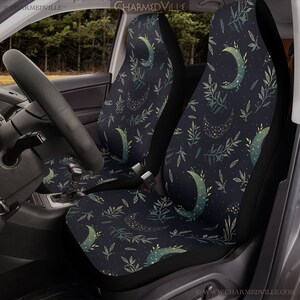 May include: A pair of black car seat covers with a repeating pattern of crescent moons, green leaves, and gold glitter. The pattern is on a dark blue background.
