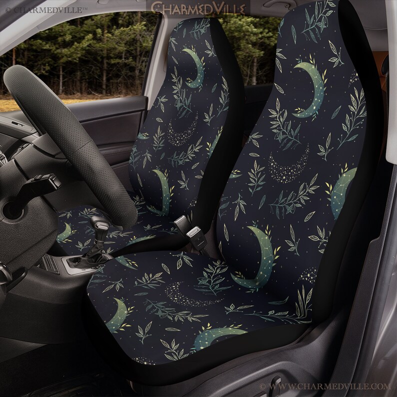 May include: A pair of black car seat covers with a repeating pattern of crescent moons, green leaves, and gold glitter. The pattern is on a dark blue background.