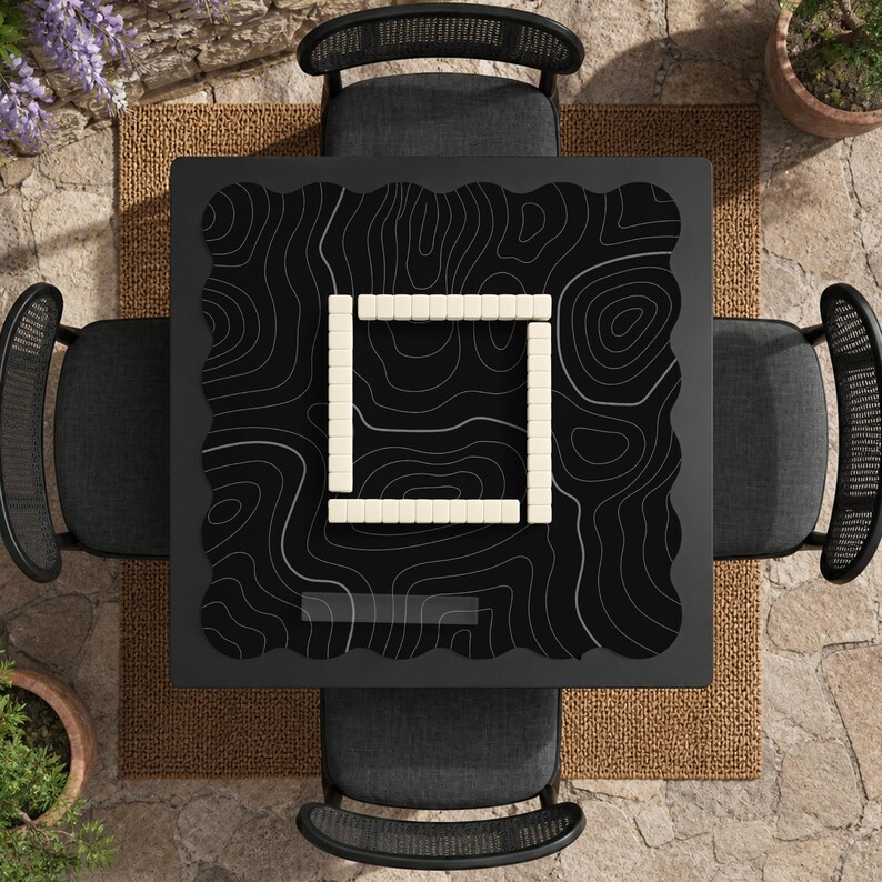 Pu&ograve; includere: Un tavolo quadrato nero con un motivo a linee topografiche bianche sulla superficie. Al centro del tavolo &egrave; disposta una composizione quadrata di tessere da gioco rettangolari color bianco sporco. Quattro sedie grigio scuro con schienali curvi lo circondano.