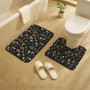 Puede incluir: Un juego de baño con una alfombra de baño rectangular y una alfombra de inodoro en forma de U. Ambas alfombras tienen un fondo negro con un patrón repetido de setas, hojas y flores. Dos zapatillas blancas están en el suelo.