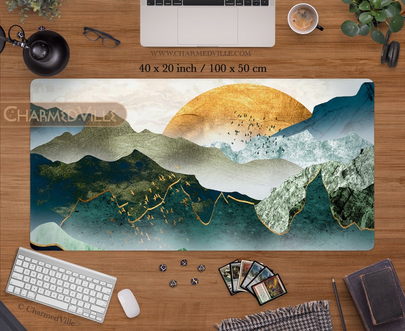 May include: A large, rectangular, white gaming mat with a blue, green, and gold abstract mountain landscape design. The design features a large, gold sun in the upper right corner and a flock of birds flying over the mountains. The mat is 40 inches by 20 inches, or 100 centimeters by 50 centimeters.