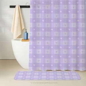May include: A lilac and white checkered shower curtain and matching bath mat. The pattern includes hearts, flowers, and sprigs. The text "CHARMEDVILLE" and "WWW.CHARMEDVILLE.COM" are visible.