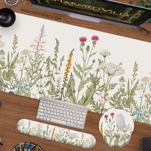 Op de afbeelding: Een witte bureauonderlegger met een bloemenontwerp met verschillende wilde bloemen, waaronder distels, madeliefjes en varens. De onderlegger wordt geleverd met een bijpassende muismat en polsrust.