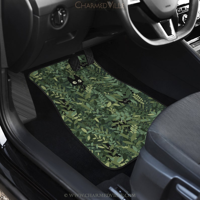 May include: Green car floor mats with a black cat pattern. The cat is peeking out from behind green leaves. The mats have the text "www.charmedville.com" on the bottom.