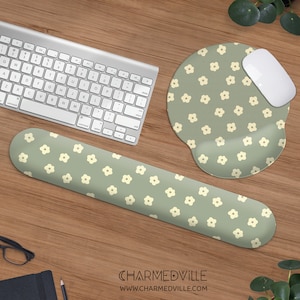 May include: A set of three desk accessories featuring a green and white floral pattern. The set includes a wrist rest, a mouse mat, and a mouse. The mouse mat is shaped like a cloud. The wrist rest is a long, rectangular shape. The mouse is white and has a rounded shape.