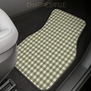May include: A car floor mat featuring a sage green and white gingham check pattern. The mat has a black border and is positioned in the footwell of a vehicle. The text CHARMEDVILLE is visible at the top center of the image in a thin font.