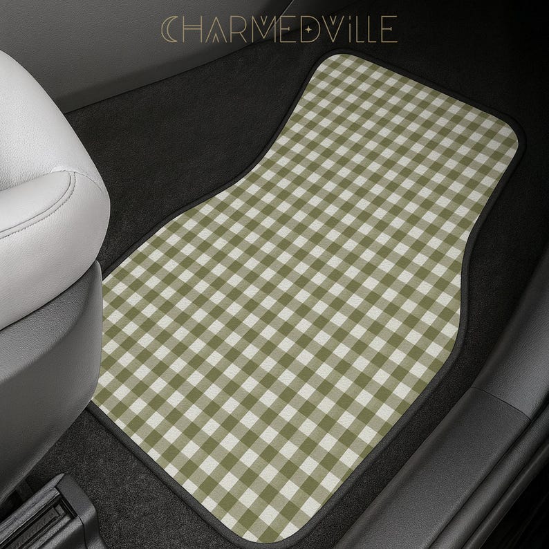May include: A car floor mat featuring a sage green and white gingham check pattern. The mat has a black border and is positioned in the footwell of a vehicle. The text CHARMEDVILLE is visible at the top center of the image in a thin font.
