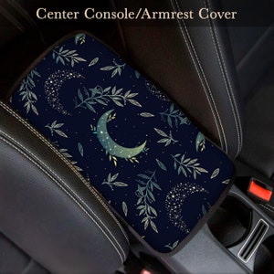 May include: A navy blue car armrest cover with a crescent moon and leaf pattern. The pattern features a constellation of stars within the moon and leaves.