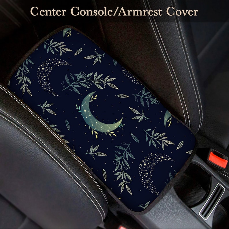 May include: A navy blue car armrest cover with a crescent moon and leaf pattern. The pattern features a constellation of stars within the moon and leaves.