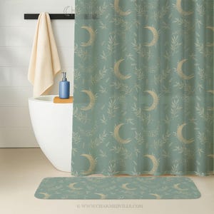 May include: A sage green shower curtain and matching bath mat featuring a repeating pattern of crescent moons and leafy branches in a light gold color. The bath set is designed for a bathroom.