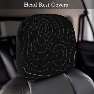 Peut inclure: Housse d'appui-t&ecirc;te noire avec un motif de carte topographique blanc. L'appui-t&ecirc;te est sur un si&egrave;ge de voiture noir. Le texte "Head Rest Covers" est en haut de l'image.
