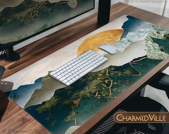 May include: A desk mat with a blue, green, and gold abstract mountain design. The mat features a gold and white sunburst pattern in the upper right corner. A white wireless keyboard and mouse are on the mat. The text "CHARMEDVILLE" is in the lower right corner.