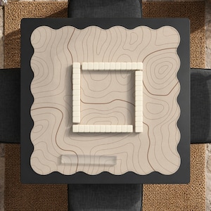 May include: A square mahjong table with a black frame and a beige playing surface. The surface features a topographic map design in brown. A square of ivory-colored mahjong tiles is in the center. The table is set on a dark gray surface.