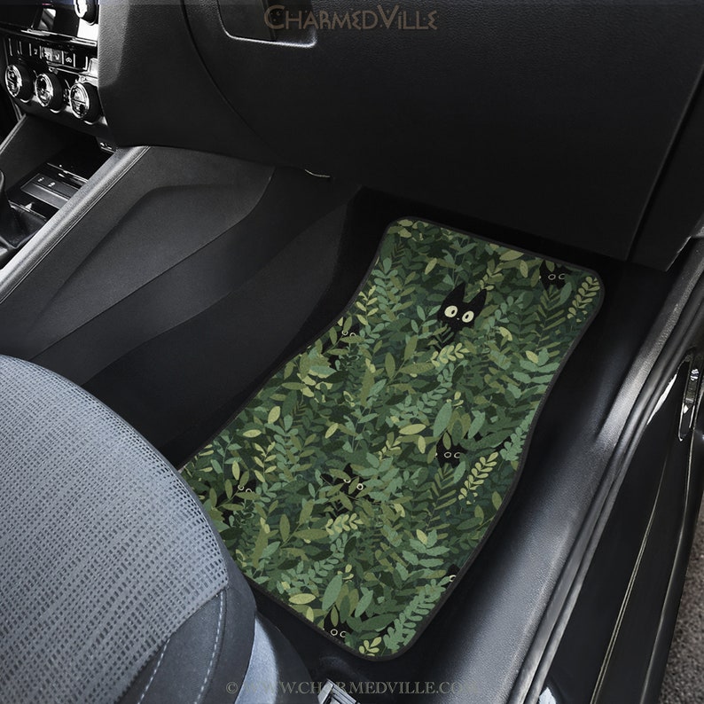 May include: Green car floor mat with a black cat peeking out from behind green leaves. The cat has large, white eyes. The mat has the text "CHARMEDVILLE" at the top.