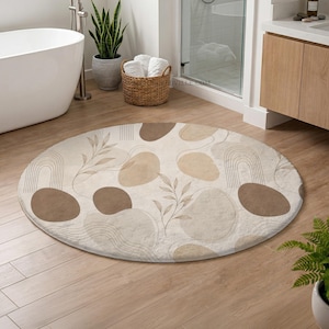 May include: A round beige bathroom rug with a modern abstract design. The rug features brown and tan organic shapes, arched lines, and leaf patterns. The rug is placed on a light wood floor, near a bathtub and a shower.