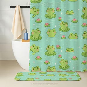 May include: A teal shower curtain and matching bath mat featuring a repeating pattern of cartoon frogs on lily pads, with pink water lilies and sparkling accents. The bathroom also includes a white tub, a beige towel, and a blue soap dispenser.