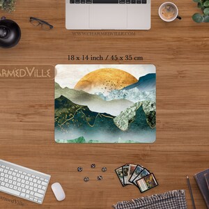 May include: A mouse pad featuring a digital illustration of a mountain range with a golden sun rising over the peaks. The mountains are a mix of green and blue hues with gold accents. The mouse pad measures 18 x 14 inches.