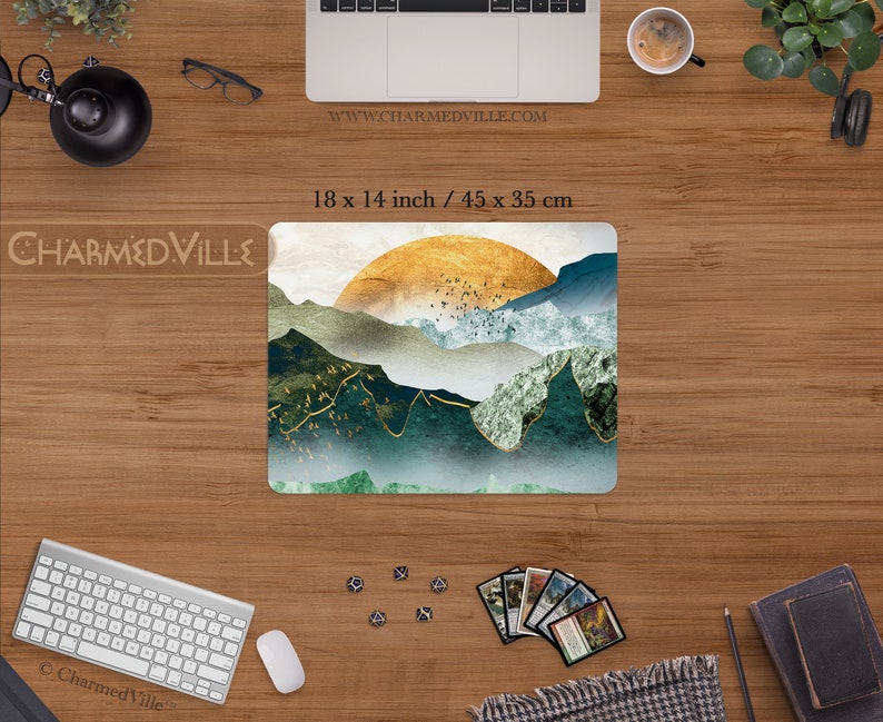 May include: A mouse pad featuring a digital illustration of a mountain range with a golden sun rising over the peaks. The mountains are a mix of green and blue hues with gold accents. The mouse pad measures 18 x 14 inches.