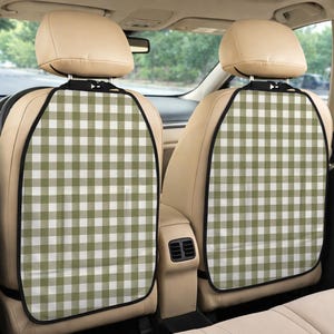 May include: Two car seat back protectors featuring a sage green and white gingham check pattern. Each protector has a black fabric border, adjustable straps at the top for headrest attachment, and a clear plastic pocket at the bottom section.