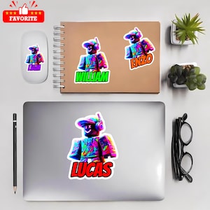 May include: A selection of vibrant stickers showcasing a digital avatar character wearing headphones and a cap. The stickers display names such as "William", "Enzo", "Lucas", and "Liam". The stickers are placed on a laptop, notebook, and mouse.