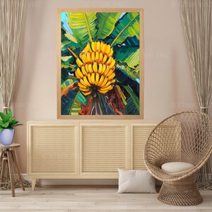 May include: A framed painting of a bunch of ripe yellow bananas with green leaves. The artwork is displayed on a light-coloured cabinet, with a woven chair and a small plant in the foreground. The painting has a natural, tropical theme.