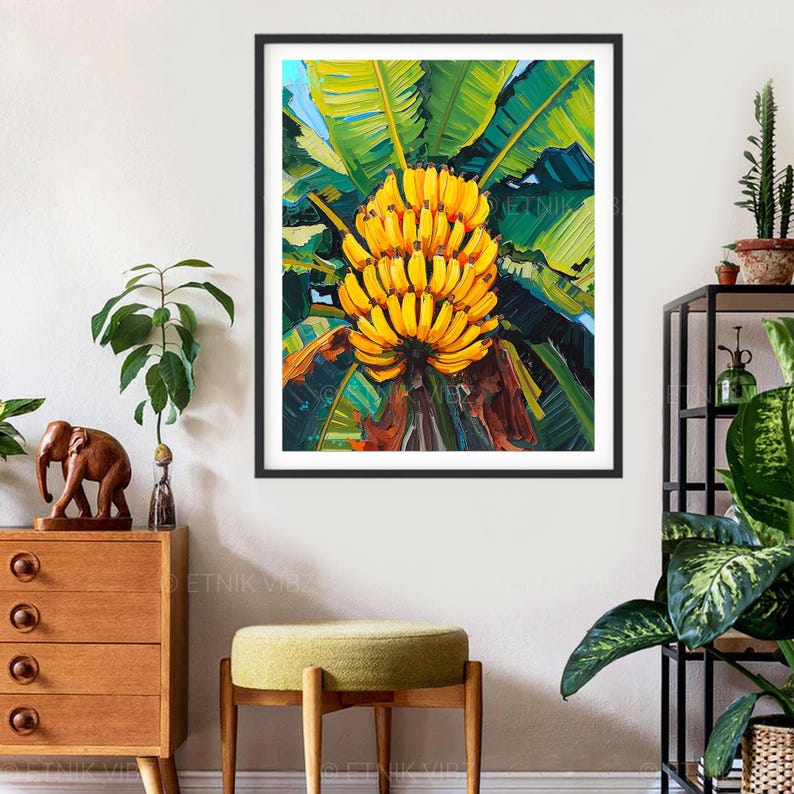May include: A framed art print depicting a painting of a bunch of yellow bananas. The bananas are surrounded by large green leaves, with a hint of blue sky visible. The artwork is set against a white wall, creating a striking contrast.