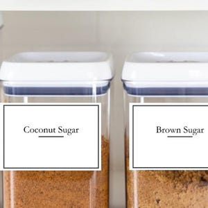 May include: Four white plastic containers with labels on the front. The labels are black with white text. The containers are filled with different ingredients, including flour, coconut sugar, brown sugar, and coconut.