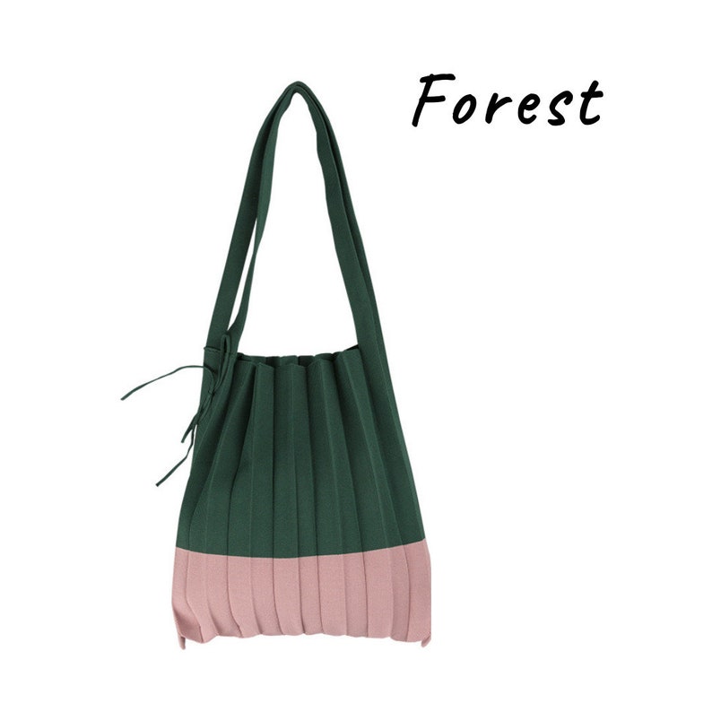 May include: A green and pink pleated tote bag with a long strap. The bag has a forest green top and a pink bottom.