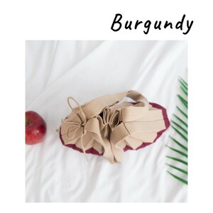 May include: A beige drawstring bag with a burgundy lining. The bag is made of a soft, pliable fabric and has a gathered, pleated design.