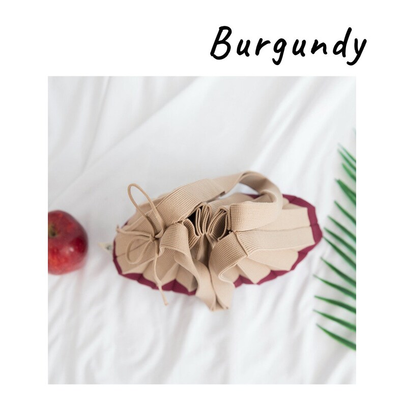 May include: A beige drawstring bag with a burgundy lining. The bag is made of a soft, pliable fabric and has a gathered, pleated design.