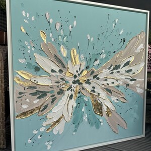 Op de afbeelding: Abstract schilderij met een blauwe achtergrond en witte, gouden en bruine accenten. Het schilderij toont een grote, gestileerde bloem met een uitbarsting van bloemblaadjes.