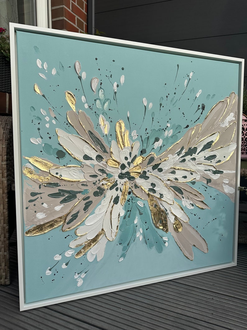 Op de afbeelding: Abstract schilderij met een blauwe achtergrond en witte, gouden en bruine accenten. Het schilderij toont een grote, gestileerde bloem met een uitbarsting van bloemblaadjes.