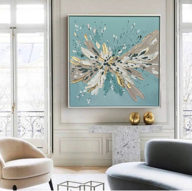 Op de afbeelding: Abstract schilderij met een groot, wit, goud en turquoise bloemmotief op een lichtblauwe achtergrond.