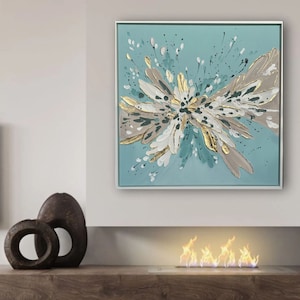 Op de afbeelding: Abstract schilderij in wit, goud en turquoise kleurschema. Het schilderij heeft een grote, centrale kleurstoot met kleinere kleurstootjes die naar buiten stralen. Het schilderij is ingelijst in een wit frame.