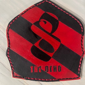 May include: A black and red leather patch with a stylized number eight and the text "THE OCHO" in red.